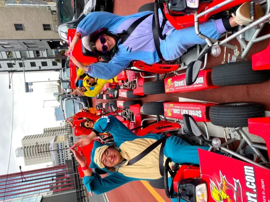 Group of people in red go-karts parked on a city street, smiling and waving at the camera.